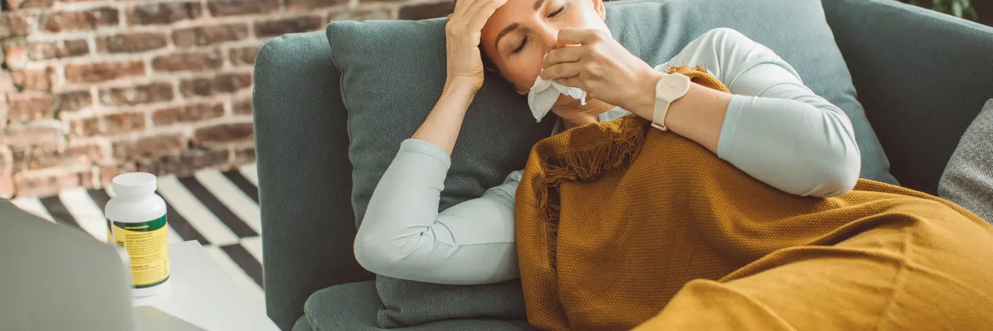 Frau auf einem Sofa mit Taschentuch vor dem Gesicht
