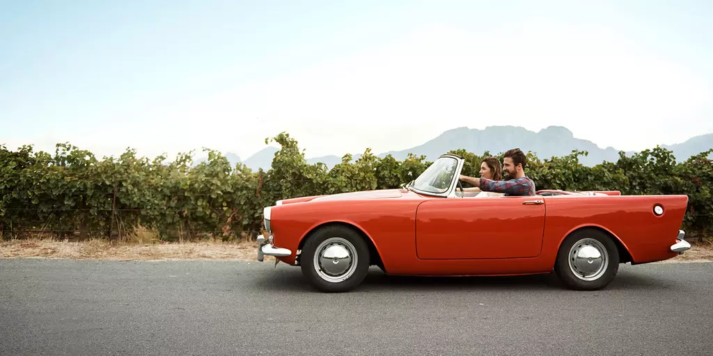 Ein junges Paar in einem roten Sport-Cabrio in südlicher Landschaft
