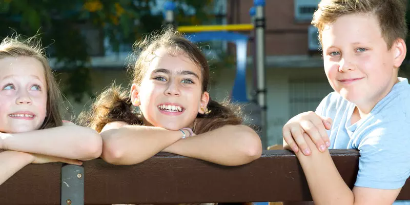 Lachende Kinder, die sich auf die Lehne einer Parkbank stützen