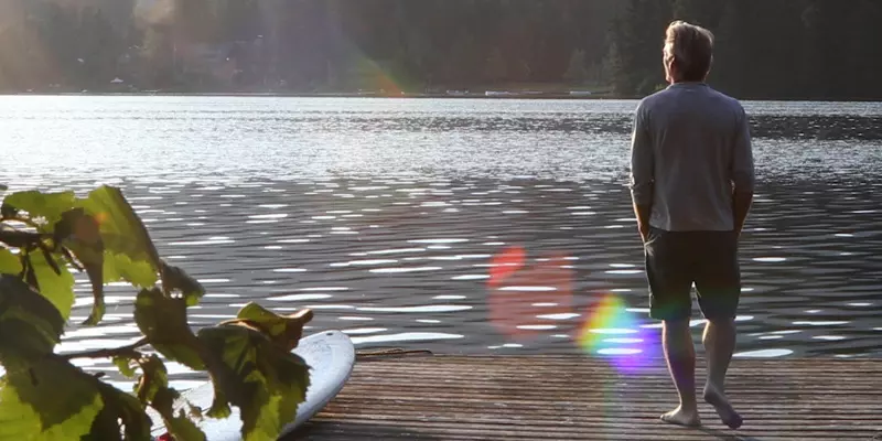 Ein Mann von hinten der an einem See auf einem Holzsteg steht