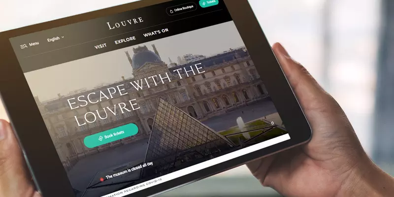 Aufsicht auf ein Tablet mit der Website des Louvre, dass eine junge Frau in den Händen hält