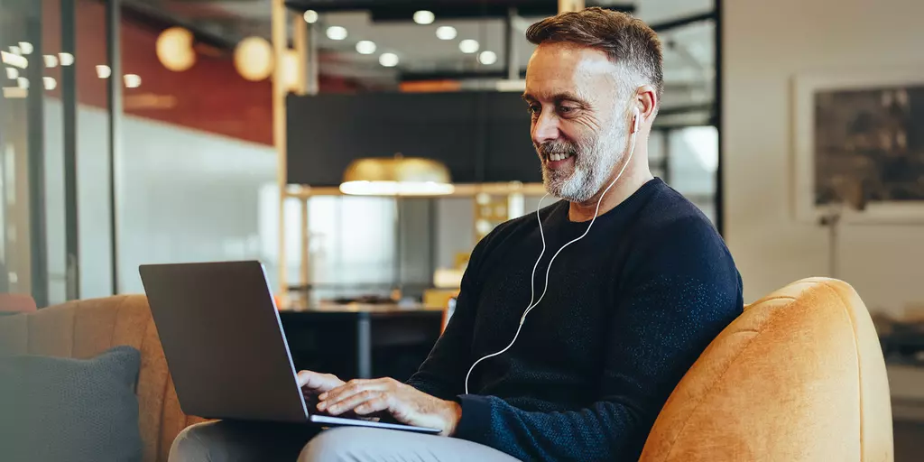 Mann sitzt auf einem Sessel und hört über Kopfhörer einen Podcast auf seinem Laptop