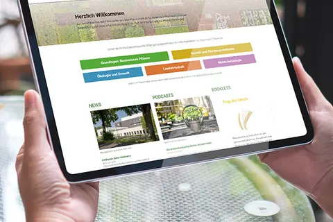 Aufsicht auf ein Tablet mit der Webseite "komm-ins-beet.mpg", das eine junge Frau in den Händen hält
