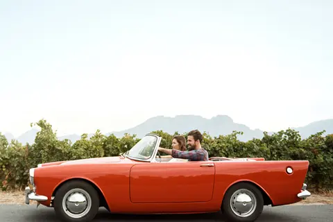 Ein junges Paar in einem roten Sport-Cabrio in südlicher Landschaft