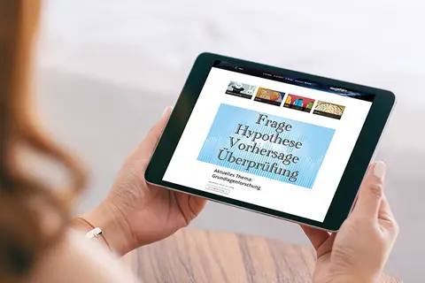 Aufsicht auf ein Tablet mit der Website "dasgehirn.info", das eine junge Frau in den Händen hält