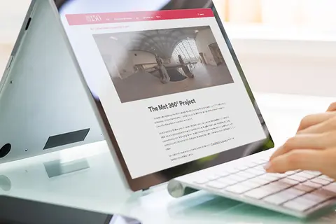 Aufsicht auf ein Laptop mit geöffneter Website des Metropolitan Museum of Art, auf dem eine Frau auf der Tastatur tippt
