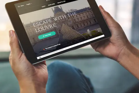 Aufsicht auf ein Tablet mit der Website des Louvre, dass eine junge Frau in den Händen hält