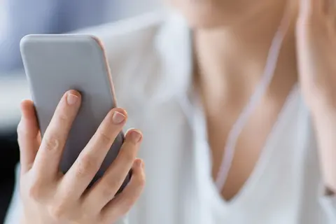 Eine junge Frau hört mit einem Kopfhörer einen Podcast auf Ihrem Smartphone