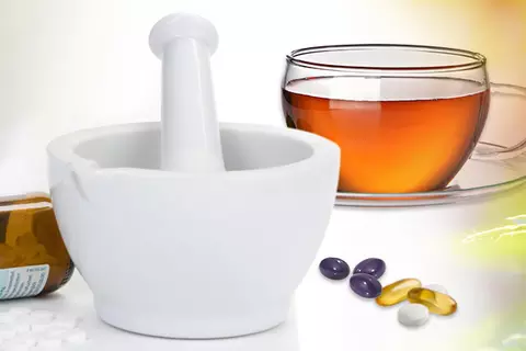 Mörser, Globuli-Flasche, Teetasse und lose Kapseln und Tabletten vor einem Bildcomposing aus Heilpflanzen 