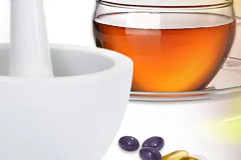Mörser, Globuli-Flasche, Teetasse und lose Kapseln und Tabletten vor einem Bildcomposing aus Heilpflanzen 