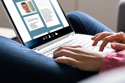 Aufsicht auf ein Laptop mit geöffneter Website der Interessensgemeinschaft „Integrative Liste Bayern“, die sich eine junge Frau anschaut