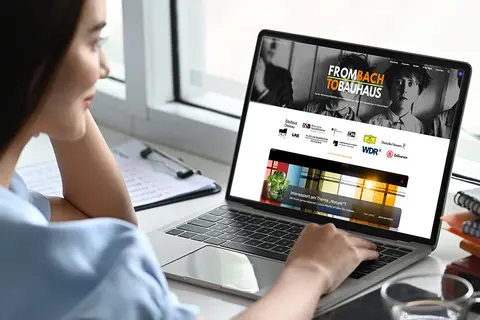 Aufsicht auf ein Laptop mit geöffneter Website artsandculture.google.com, die sich eine junge Frau anschaut