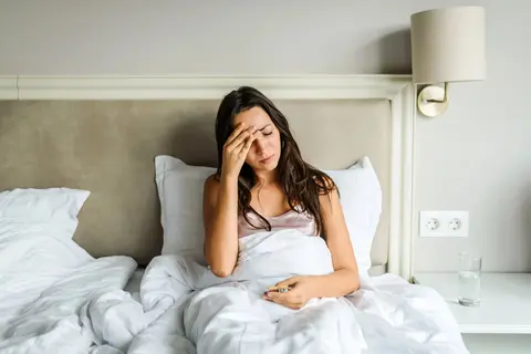 Junge Frau im Bett hält die Hand an der Schläfe
