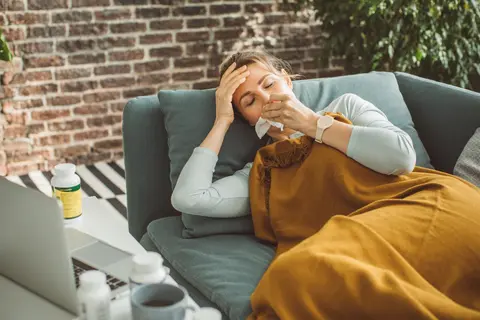 Frau auf einem Sofa mit Taschentuch vor dem Gesicht