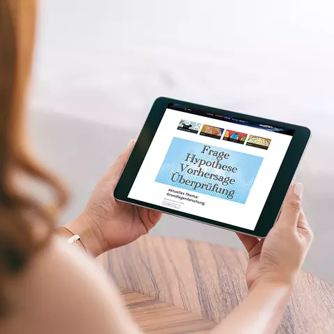 Aufsicht auf ein Tablet mit der Website "dasgehirn.info", das eine junge Frau in den Händen hält