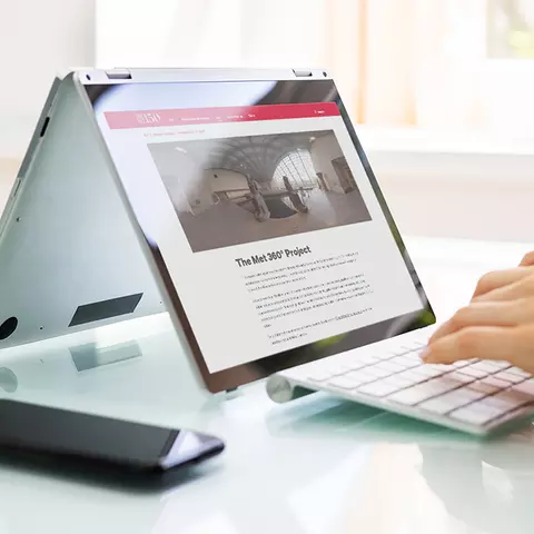 Aufsicht auf ein Laptop mit geöffneter Website des Metropolitan Museum of Art, auf dem eine Frau auf der Tastatur tippt