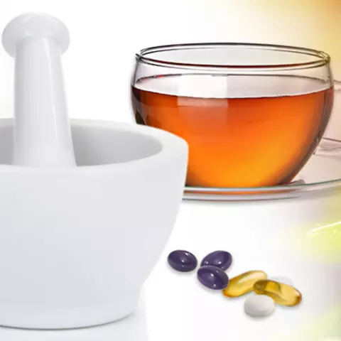 Mörser, Globuli-Flasche, Teetasse und lose Kapseln und Tabletten vor einem Bildcomposing aus Heilpflanzen 