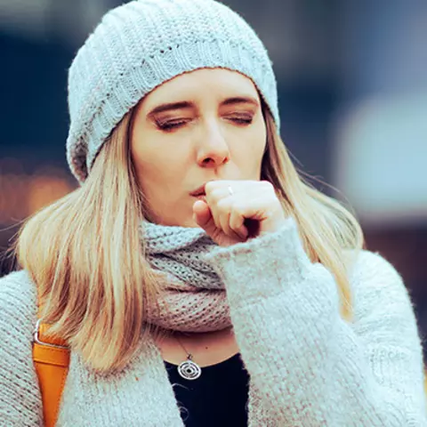 Junge Frau, die sich wegen einer Bronchitis in die Faust hustet