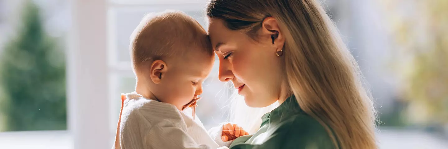 Mutter hält ein Baby im Arm, beide berühren sich zärtlich Stirn an Stirn.
