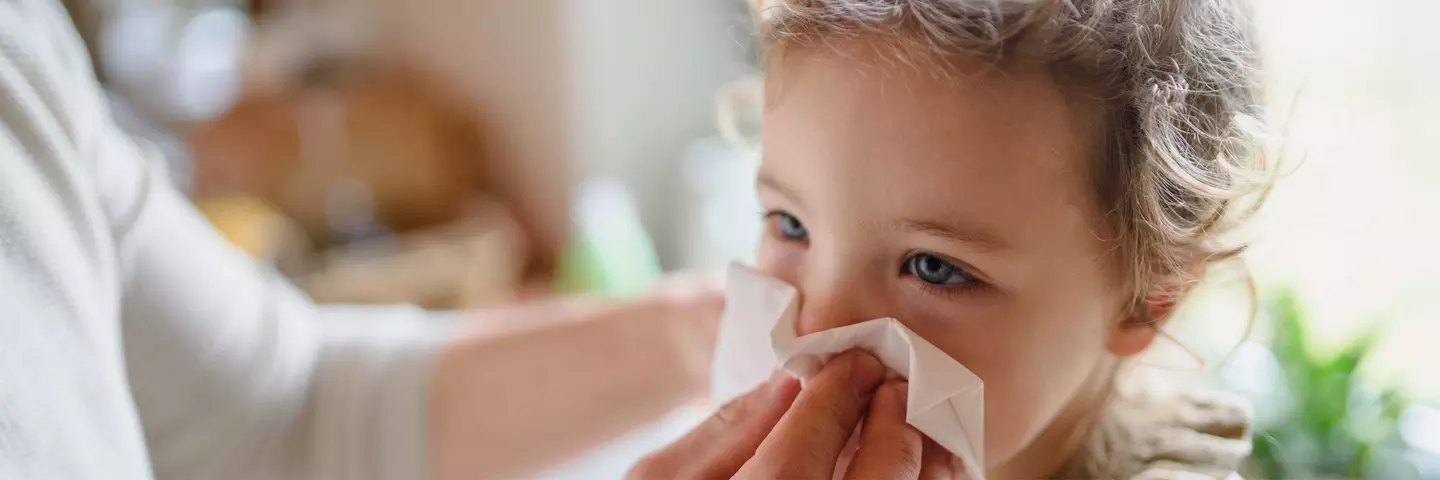 Eine erwachsene Person wischt einem Kind die Nase mit einem Tuch ab.