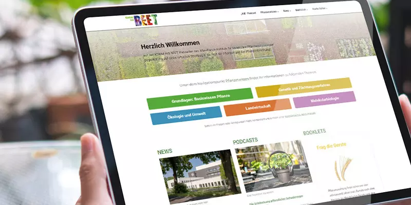 Aufsicht auf ein Tablet mit der Webseite "komm-ins-beet.mpg", das eine junge Frau in den Händen hält