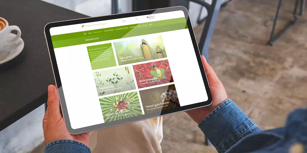 Aufsicht auf ein Tablet mit der Website "Plantainment", dass eine Junge Frau in den Händen hält