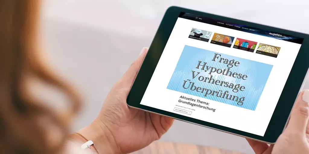 Aufsicht auf ein Tablet mit der Website "dasgehirn.info", das eine junge Frau in den Händen hält