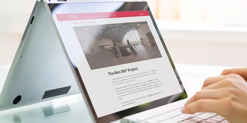 Aufsicht auf ein Laptop mit geöffneter Website des Metropolitan Museum of Art, auf dem eine Frau auf der Tastatur tippt
