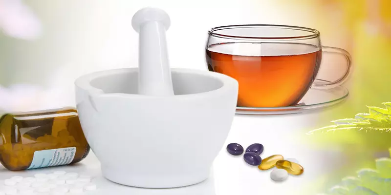Mörser, Globuli-Flasche, Teetasse und lose Kapseln und Tabletten vor einem Bildcomposing aus Heilpflanzen