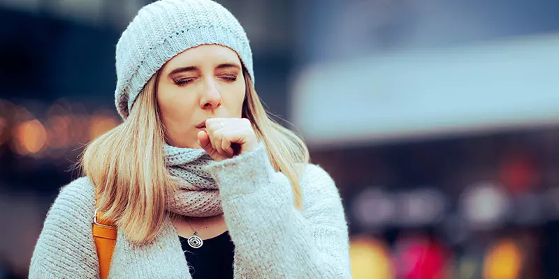 Junge Frau, die sich wegen einer Bronchitis in die Faust hustet