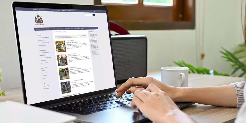Aufsicht auf ein Laptop mit geöffneter Website des Märchenatlas, auf dem eine Frau auf der Tastatur tippt