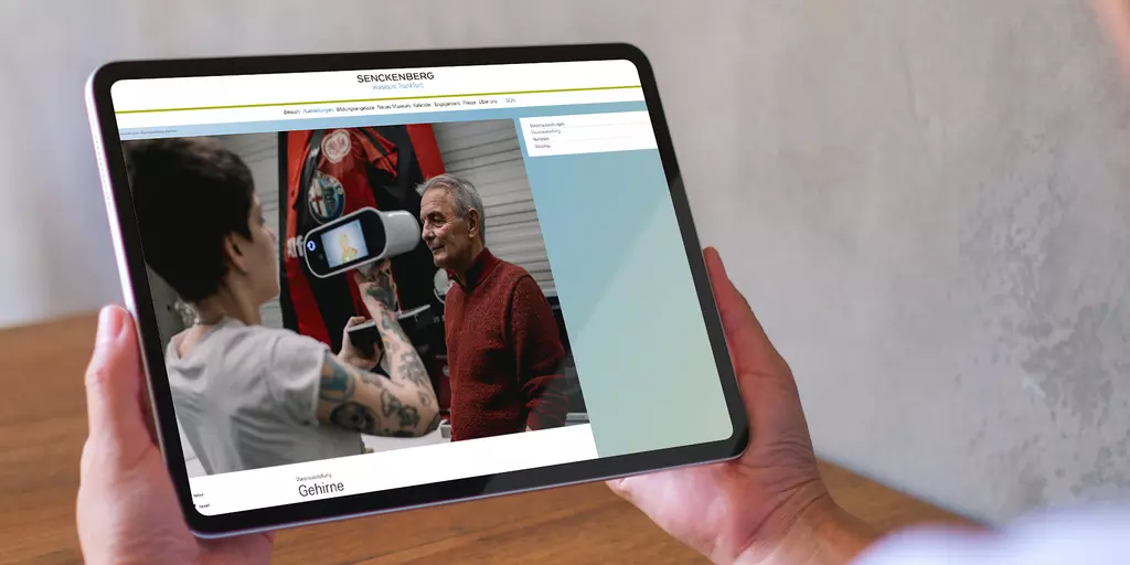 Aufsicht auf ein Tablet mit geöffneter Website des Senckenberg Museums, dass eine junge Frau in den Händen hält