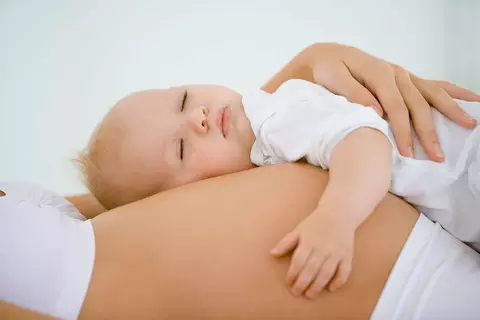 Bauch einer schwangeren Frau auf dem ein schlafendes Kleinkind liegt