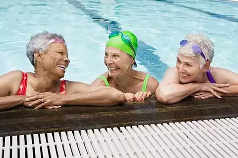 Drei Damen stützen sich am Schwimmbeckenrand ab und unterhalten sich