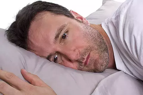 Mann liegt mit offenen Augen im Bett und leidet an Schlafstörungen