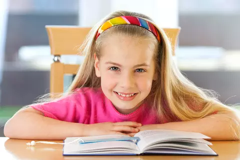 Lachendes Mädchen sitzt vor Ihrem Schulbuch