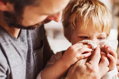 Vater mit Kind, dass in ein Taschentuch schneuzt