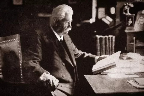 Herr Dr Willmar Schwabe sitzt an Schreibtisch mit Buch und liest