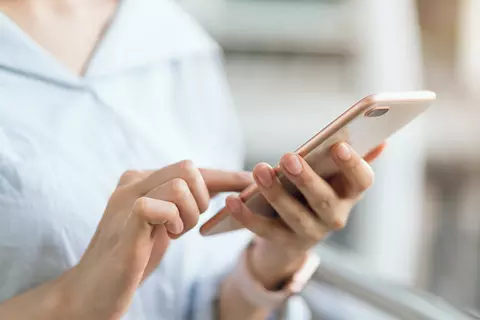 Detailaufnahme der Hände einer jungen Frau die auf ihrem Smartphone tippt