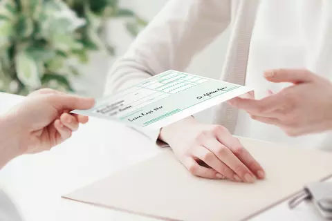Detailaufnahme der Hände einer Ärztin, die einer Patientin ein grünes Rezepz übergibt