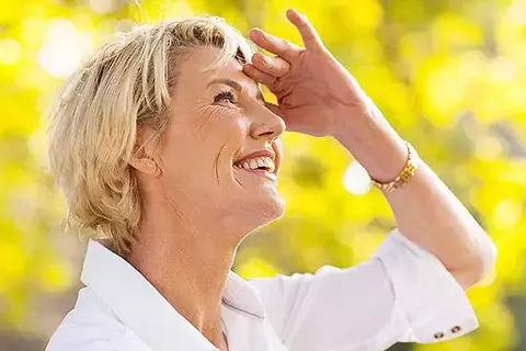 Ältere Dame schut lächelnd in die Sonne und schirmt dabei Ihre Augen mit der Hand ab