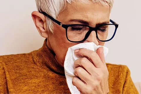 Ältere Dame mit Brille schneuzt sich die Nase