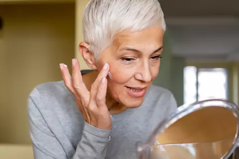 Ältere Frau cremt sich im Gesicht ein