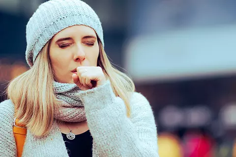 Junge Frau, die sich wegen einer Bronchitis in die Faust hustet