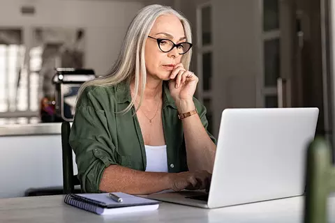 Frau sitzt an ihrem Schreibtisch und macht an ihrem Laptop den Selbsttest Hämorrhoiden