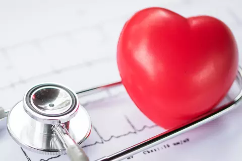 Stilleben aus Stethoskop und einem Modellherz auf ausgedruckten EKG-Kurven