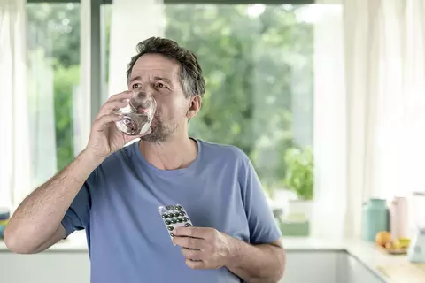 Ein Mann hält einen Tablettenblister in der Hand und trinkt Wasser aus einem Glas