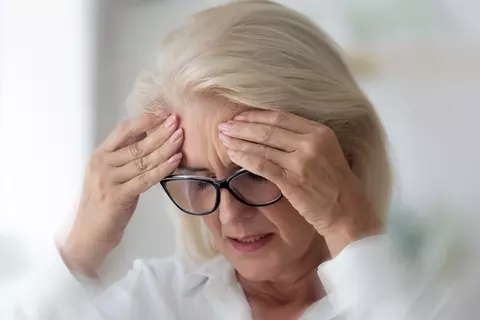 Frau mit Brille hält aufgrund von Schwindel ihren Kopf in den Händen
