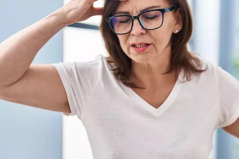 Eine Frau greift sich wegen Schwindel mit der einen Hand an den Kopf und stützt sich mit der anderen an einem Schrank ab