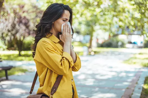 Frau im gelben Mantel schnäuzt sich mit einem Taschentuch in einem Park.